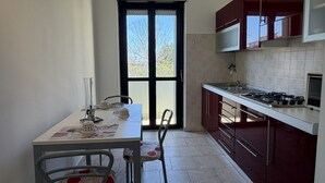 A kitchen with a dining table, chairs, a stove, cabinets, and a window. - Kairos - Casa Vacanze (Fuscaldo)