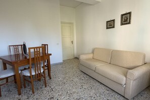 Een kamer met een eettafel en stoelen, een beige bank en twee ingelijste foto's aan de muur.