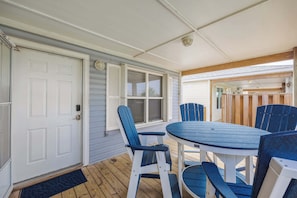 Eine überdachte Veranda mit Tisch und Stühlen, einer Tür und einem Fenster mit Fensterläden.