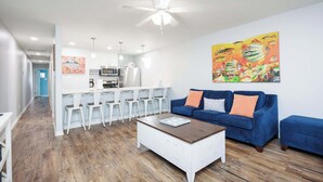 Ein modernes Wohnzimmer mit einem blauen Sofa, einem weißen Couchtisch und einer Küche im Hintergrund.