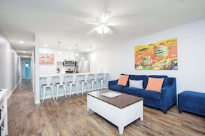Ein modernes Wohnzimmer mit einem blauen Sofa, einem weißen Couchtisch und einer Küche im Hintergrund.