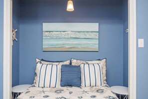 Ein Schlafzimmer mit einem Bett, einem Meeresbild, einem kleinen runden Tisch und einer Wandleuchte.