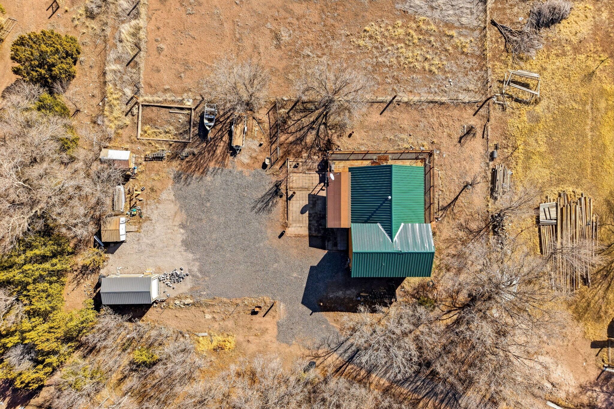 An aerial view of a property with a green-roofed building, a fenced area, and scattered structures.