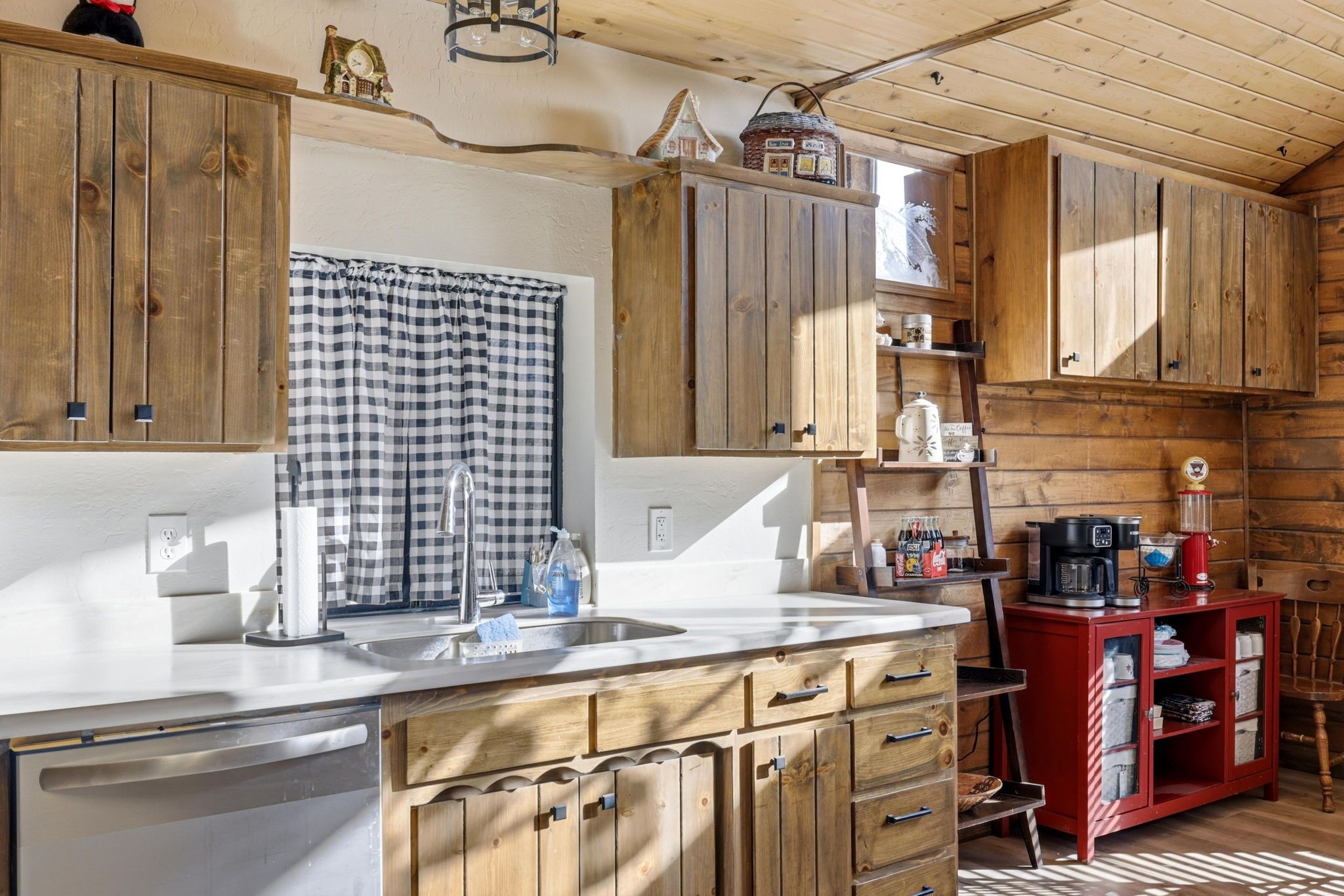 Innenansicht einer Holzhütte mit Küchenbereich, der ein Spülbecken, Schränke und ein roter Schrank mit Regalen umfasst.