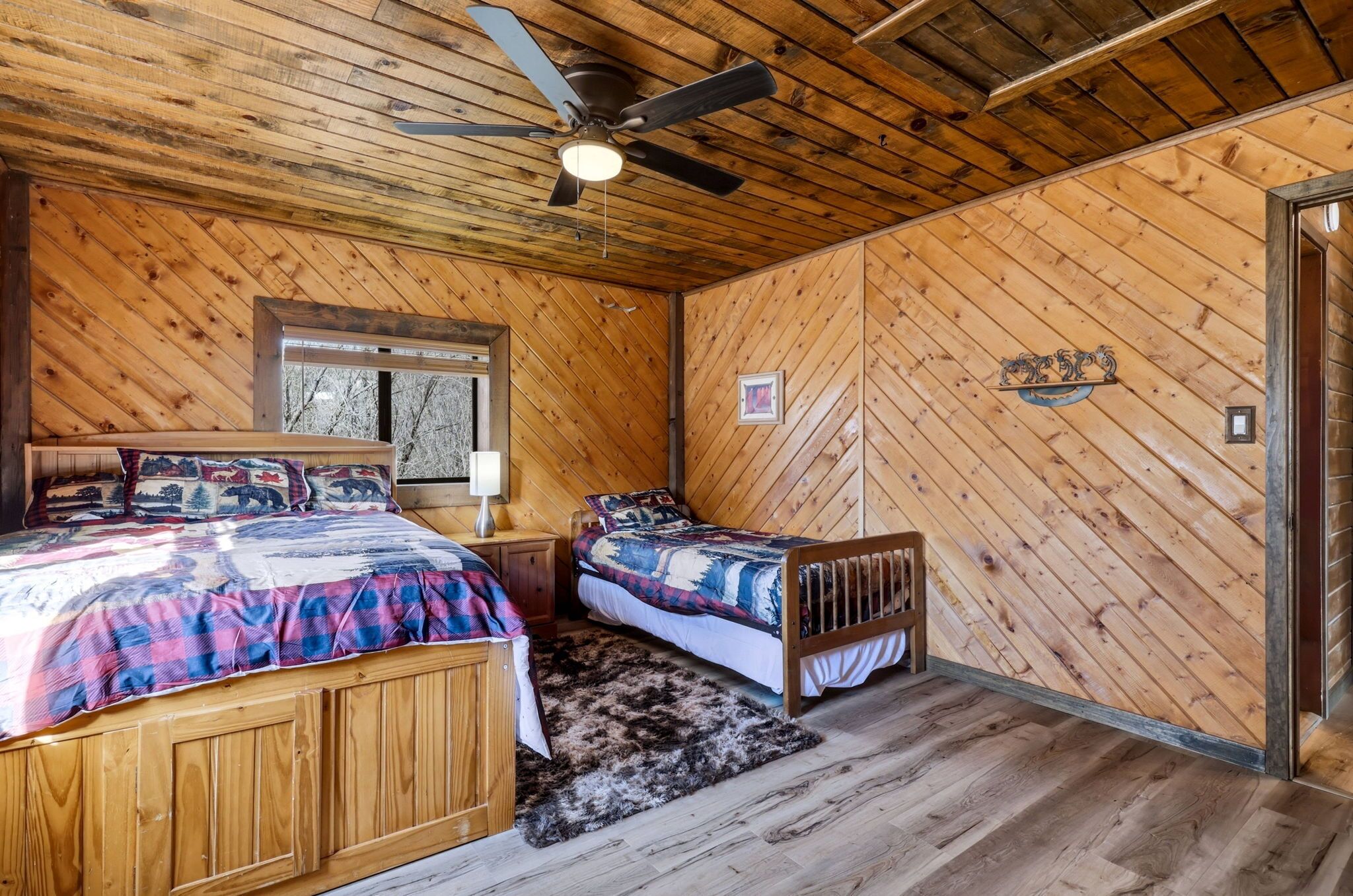 A cabin-style bedroom with two beds, a ceiling fan, wooden walls, and a window.