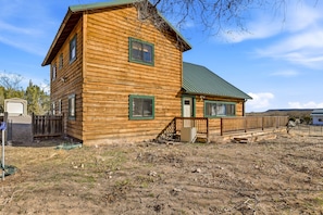 A wooden log cabin with a green roof, a front porch, and a fenced yard.