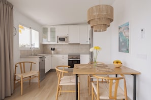 A modern kitchen with white cabinets, a microwave, and a dishwasher. There is a wooden dining table with chairs and a hanging light fixture.