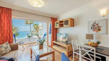 Un salon moderne avec un téléviseur, une table à manger et des chaises. Il y a un balcon avec vue sur la mer.