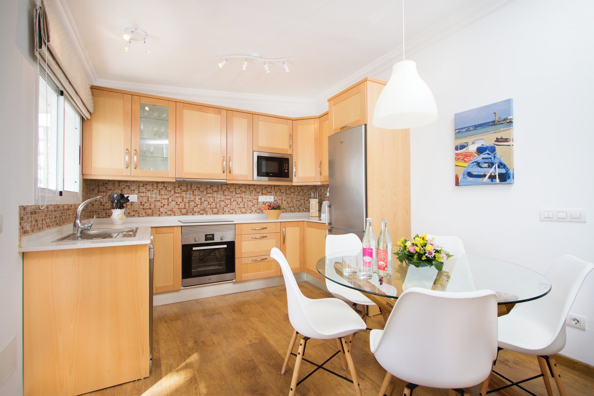 A modern kitchen with wooden cabinets, a microwave, an oven, and a glass dining table with white chairs.