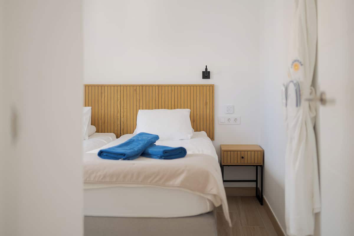 A hotel room with a wooden headboard, a bed with white linens, a small bedside table, and a white robe hanging on the wall.
