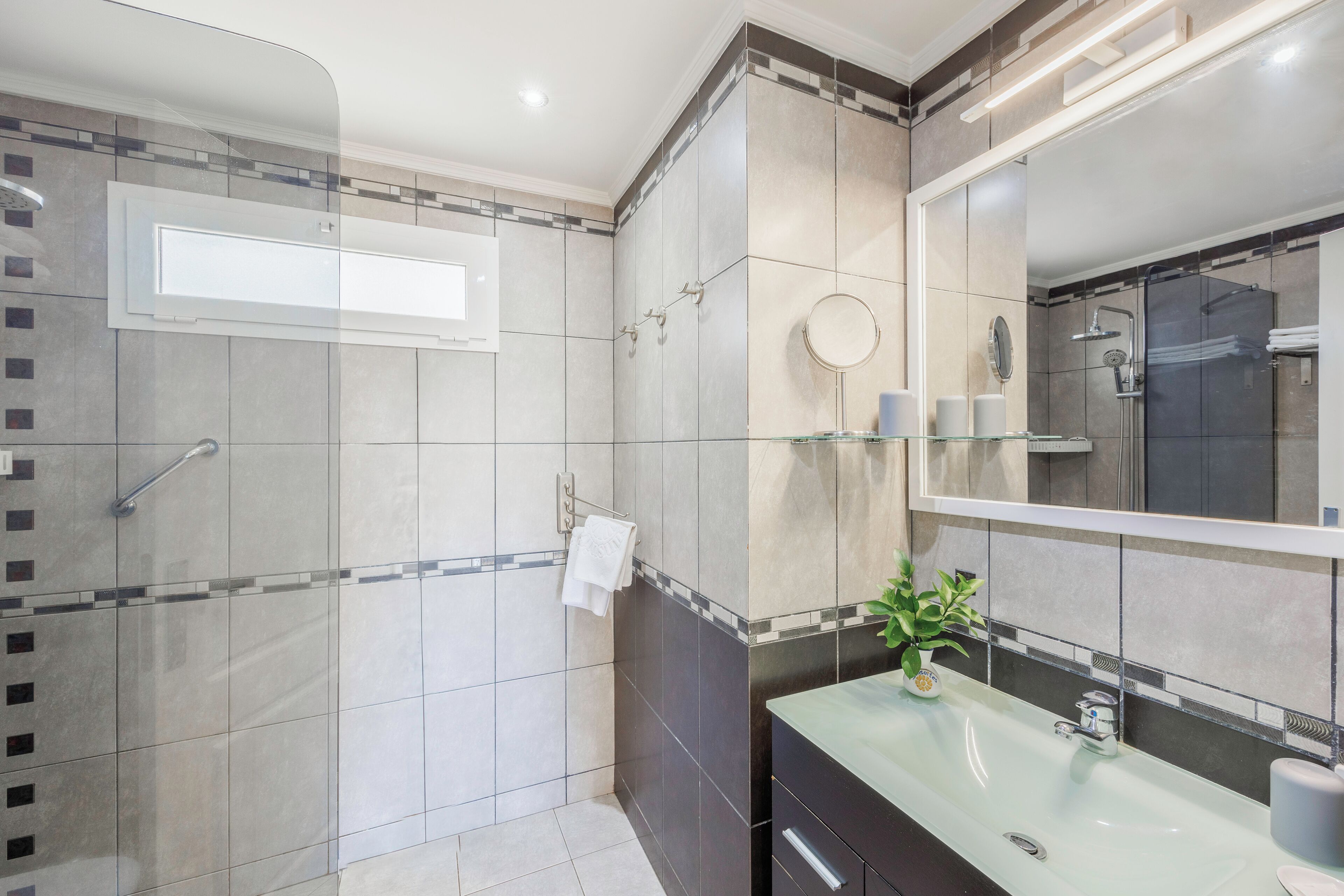 A modern bathroom with a glass shower enclosure, a vanity with a sink, and a large mirror.