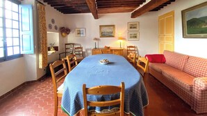 Uma sala de jantar com uma mesa redonda, cadeiras, um sofá e uma janela com cortinas.