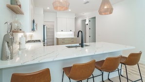 Una cocina moderna con una isla de mármol, luces colgantes y taburetes de bar.