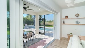 Un salón moderno con vistas a la piscina, puertas de cristal correderas, un ventilador de techo y suelo de madera.