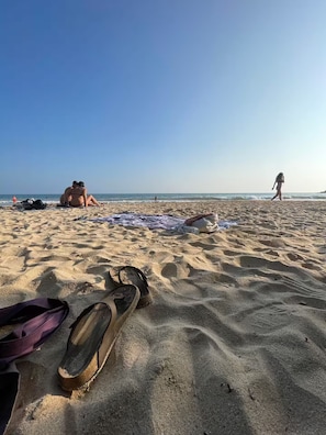 Una playa arenosa con huellas, un par de sandalias y una manta.