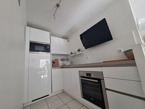A modern kitchen with white cabinetry, a microwave, an oven, and a flat-screen TV mounted on the wall. - Apartment with balcony in the heart of Le Touquet (Le Touquet-Paris-Plage)