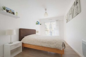 A bedroom with a bed, bedside table, lamp, and a window with a view. - Apartment with balcony in the heart of Le Touquet (Le Touquet-Paris-Plage)