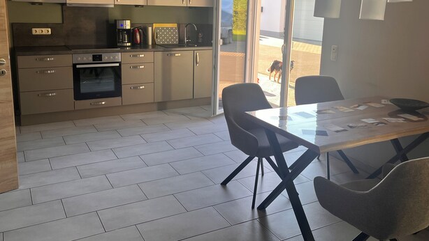 Cozinha moderna com eletrodomésticos de aço inoxidável, área de jantar com mesa de vidro e porta de correr que dá para um pátio.