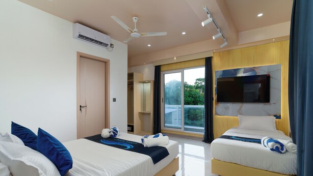 A hotel room with two beds, a ceiling fan, a flat-screen TV, and a large window with a view of greenery. - Ocean Bounty (Ukulhas)