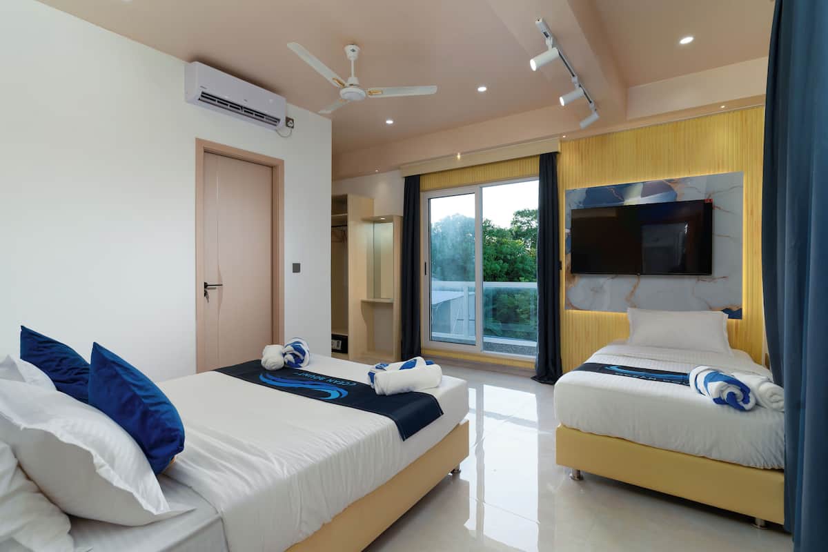 Une chambre d’hôtel avec deux lits, un ventilateur de plafond, un téléviseur à écran plat et une grande fenêtre donnant sur un paysage verdoyant.