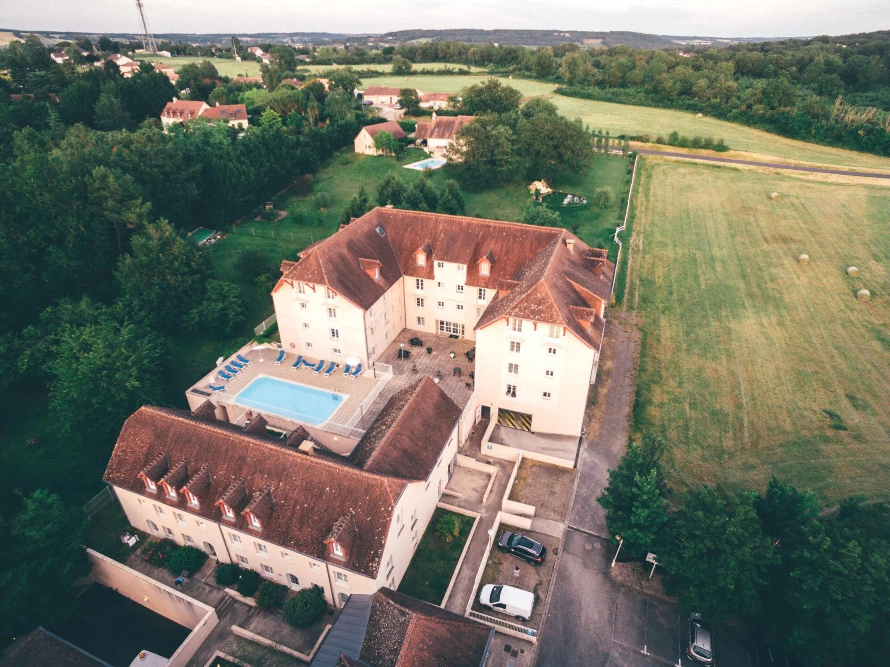 An aerial view of a large estate with multiple buildings, a swimming pool, and surrounding green fields.