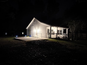 A single-story building with a porch, a visible trash bin, and a paved driveway.