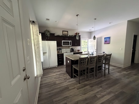 A modern kitchen with a central island, dark wood cabinets, and a white refrigerator.. 2-bedroom cottage in adorable Summerville with AC comfort