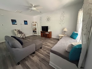 A living room with a grey sofa, a smaller grey couch, a TV stand, a bookshelf, and decorative wall art.