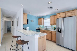 Eine Küche mit Holzschränken, einem Edelstahlkühlschrank, einer Granitabdeckung und zwei Barhocker.