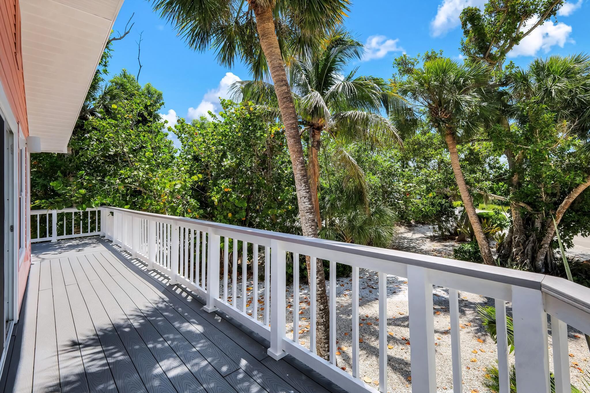 A wooden deck with white railings, surrounded by lush greenery and palm trees.