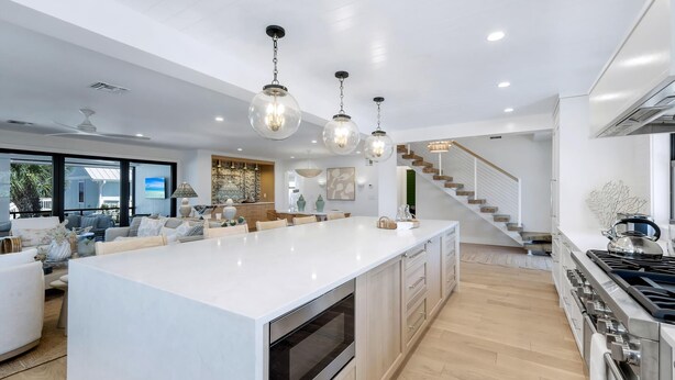 Une cuisine moderne dotée d’un grand îlot central, d’appareils électroménagers en acier inoxydable et de luminaires suspendus.
