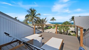 Une terrasse en bois avec des chaises longues, une pergola et une vue sur la plage et l’océan.