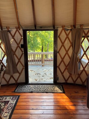 Una carpa con piso de madera, vista a árboles y una cerca en el exterior, y una felpudo con un diseño.