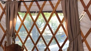 Una habitación con un separador de madera celosíaca, una silla y vistas a través de una ventana con cortinas.