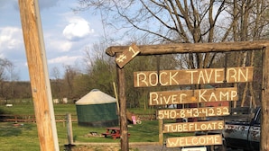 Un letrero de madera con la leyenda 'ROCK TAVERN' y 'RIVER KAMP', junto con un número de teléfono.