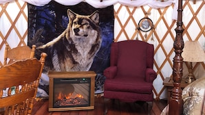 Una habitación con una silla de madera, un sillón rojo, una mesa de madera, un tapiz y una chimenea.