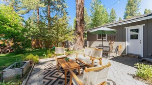 Een terras met houten meubels, een tafel en stoelen, omgeven door een tuin en een grote boom.