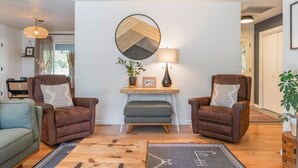 Een woonkamer met twee leren fauteuils, een tafeltje met een lamp, een ronde spiegel en een potplant.