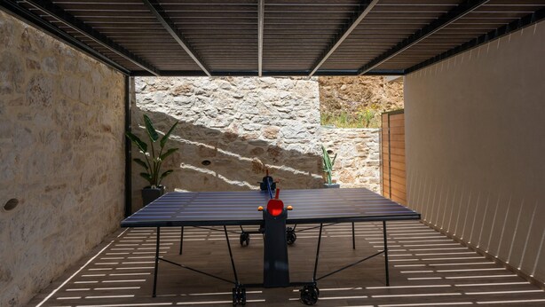 Un tavolo da ping pong in un ambiente chiuso con una parete in pietra e un tetto in metallo.