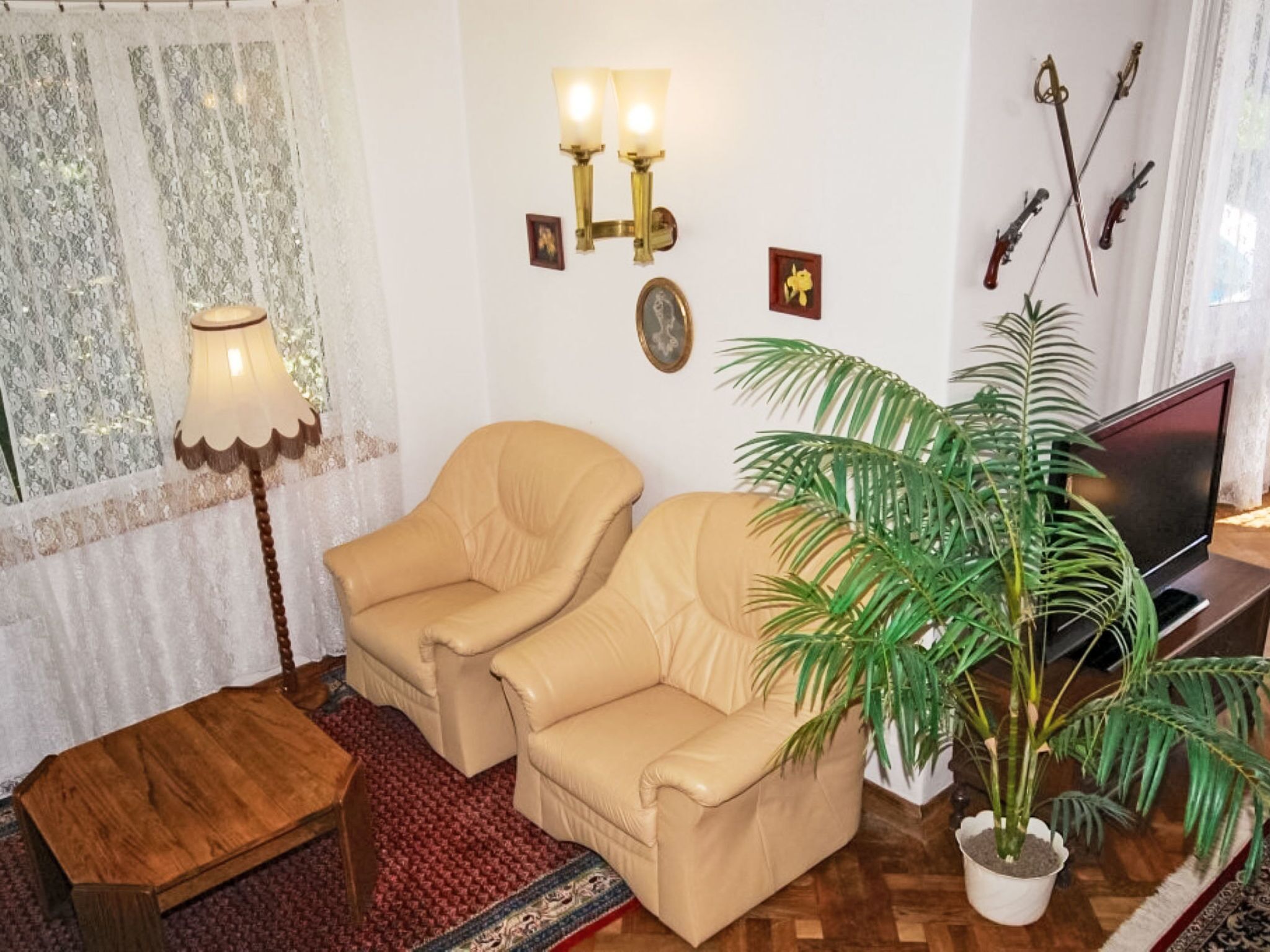 Sala de estar con dos sillones color beige, una mesa de centro de madera, televisor, planta en maceta, luces empotradas en la pared y una ventana con cortinas.