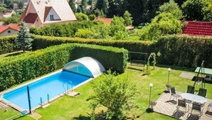 Piscina con cerramiento de vidrio, rodeada de setos cuidados y un patio con mobiliario exterior.