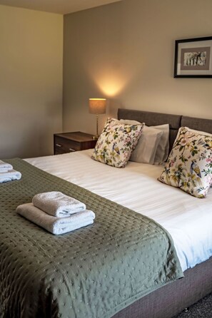 A neatly made bed with a green quilt, two pillows with a floral pattern, and a lamp on a bedside table. - Easter Caiplich by Interhome (Glenshee)