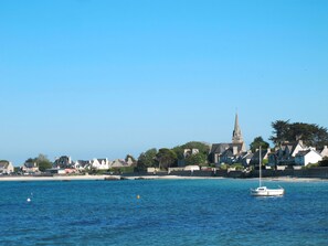 Une ville côtière avec un clocher d’église imposant, une mer calme et un petit bateau ancré près du rivage.