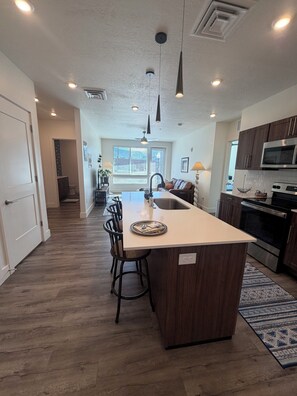 A modern kitchen with a central island, dark wooden cabinets, stainless steel appliances, and pendant lighting.
