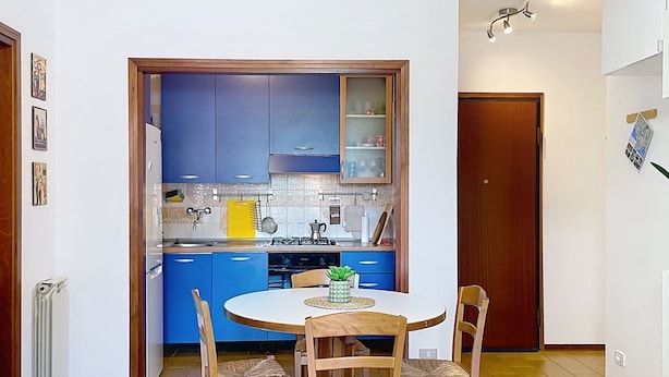 A compact kitchen with blue cabinets, a dining table with chairs, and a small island with a plant. - Casa Elena by Interhome (Bellano)