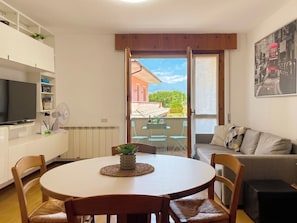 A dining area with a round table, chairs, a TV, and a balcony with a view. - Casa Elena by Interhome (Bellano)