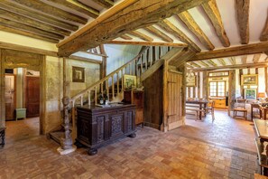 Un interior rústico con vigas de madera a la vista, una escalera y suelo de ladrillo.