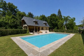 Una casa con piscina, rodeada de césped cuidado y árboles.