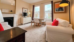 A living room with a fireplace, a dining area, and a sofa with red cushions. - Sugden Road (London)