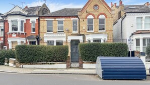 A row of terraced houses with a central building featuring a prominent bay window and a black front door. - Sugden Road (London)